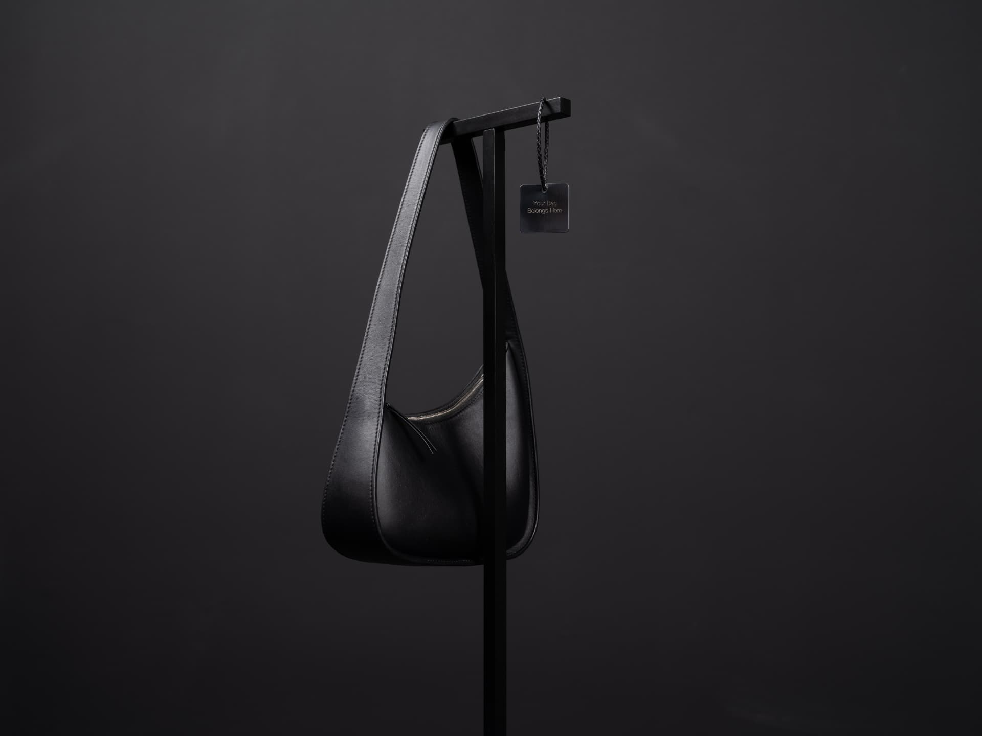 Close view of the Luxestands top bar with a leather bag strap resting across it and an engraved metal tag.