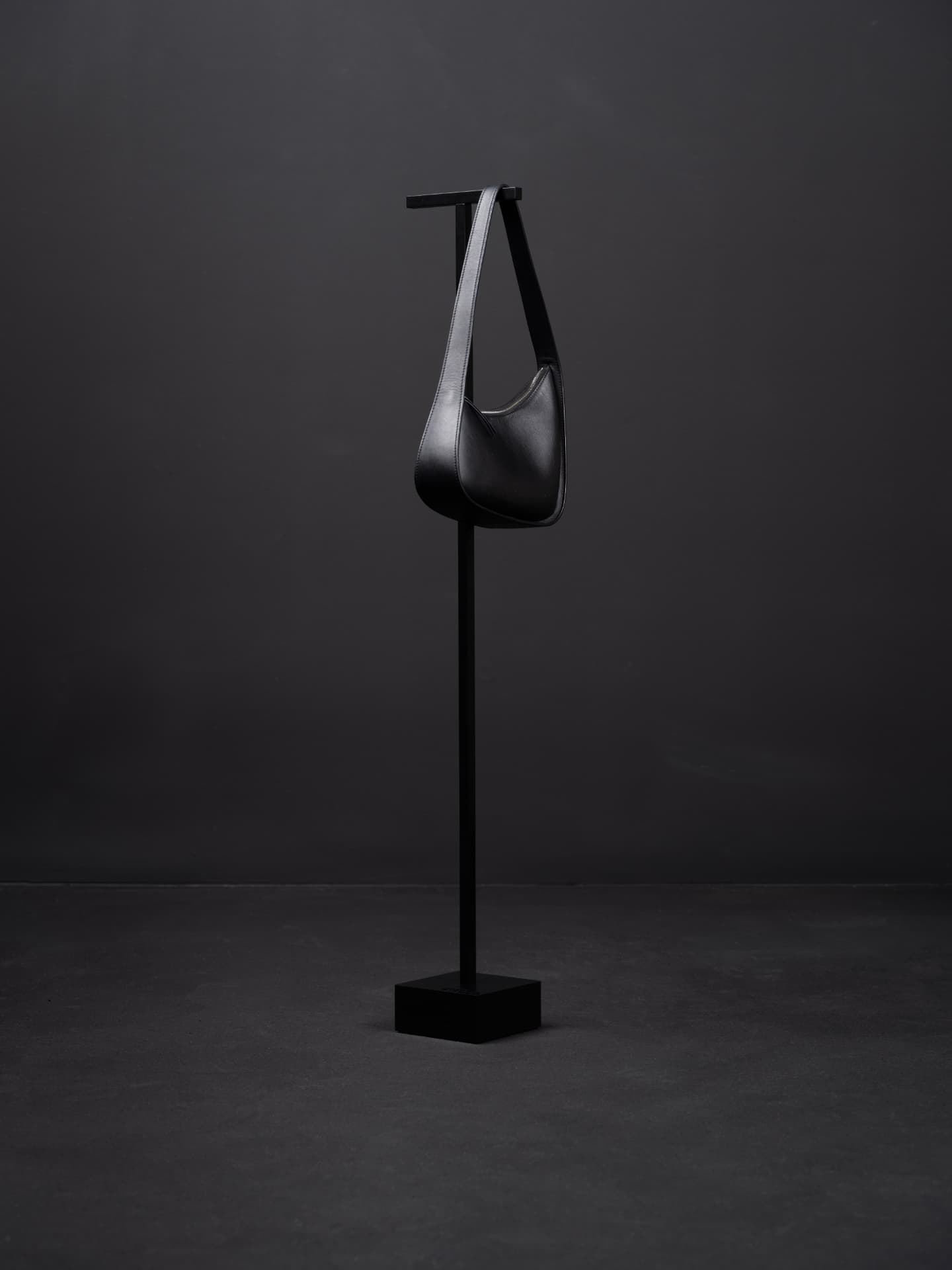 A satin-black Luxestands handbag stand holding a black leather shoulder bag in a low-lit interior.